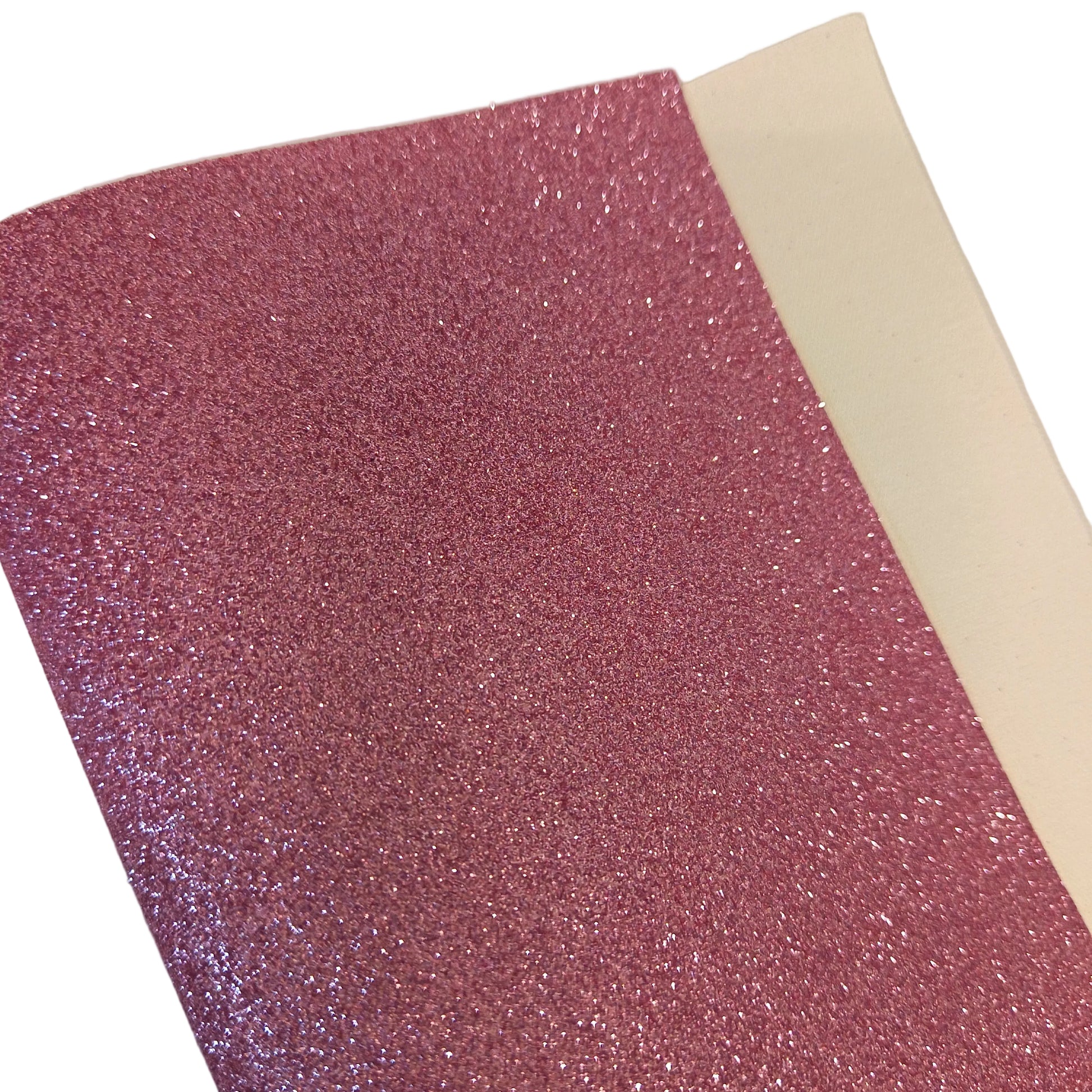 A close-up of a rectangular sheet of pink glitter material with a white backing visible along one edge, photographed on a plain light background.